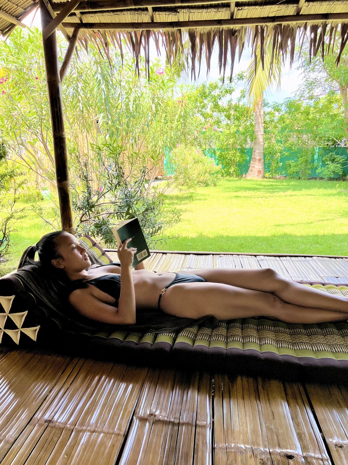 A guest reading on a Thai cushion in the bamboo sala, looking out over the garden at Vihara